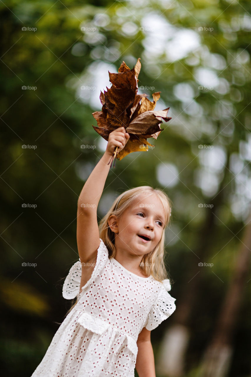 Little girl with blonde hair holding fallen leaves in the park 
