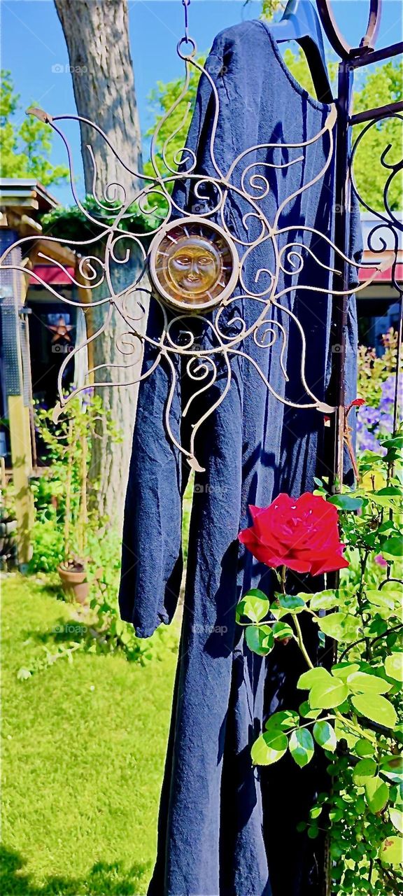 The beautiful house and garden in „Lower Bavaria“, Germany is full of eclectic collectibles, artwork and antique treasure such as this ornate sun disc next to the red roses. Behind it a long undergarment dries in the sun. 2024. Hypnotic Productions