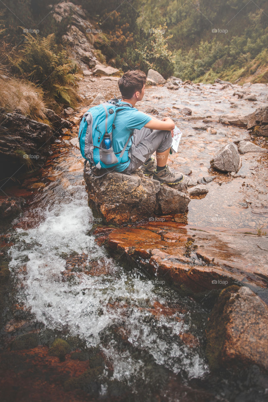 Rear view of a woman sitting on rock near flowing water