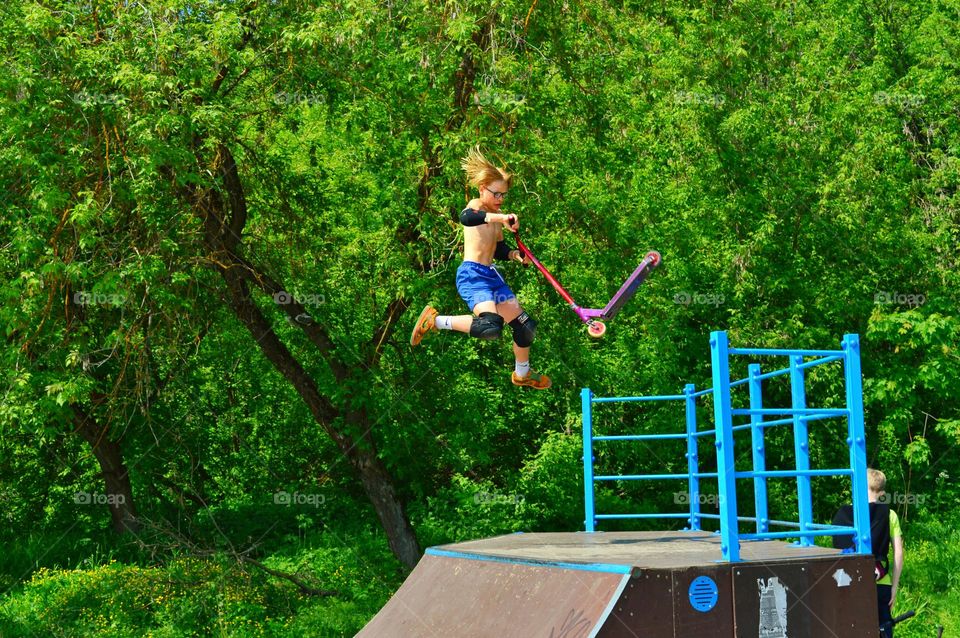 a young man performs tricks on a stunt scooter flying over a ramp