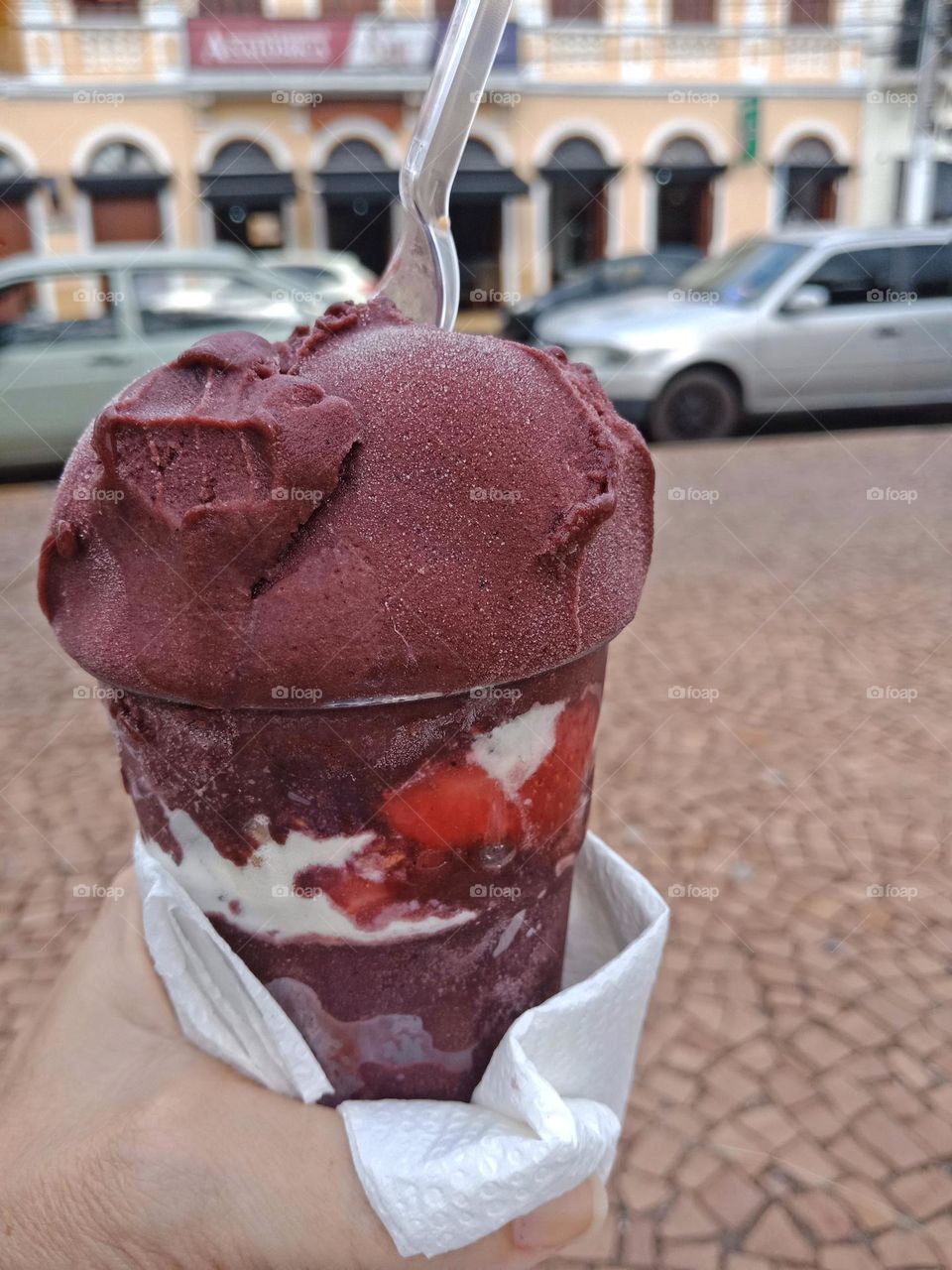 Having a cup of açaí with strawberries and milk powder on a sidewalk
