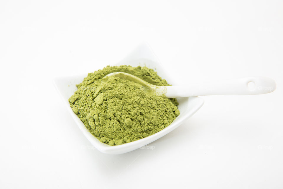 Health product - barley grass green powder in white bowl with white spoon on white background. Closeup macro image