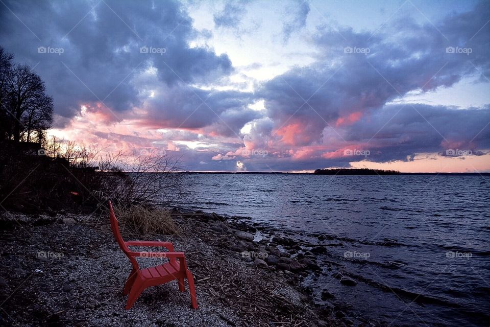 It was an early spring 2016. The ice melt came early. The sunset casting red hues onto the clouds and sky and a lone beach chair waits for visitors.