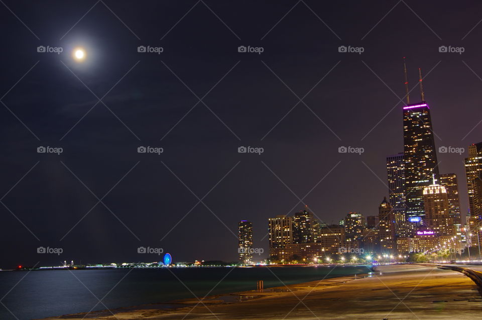 Time exposure of Chicago skyline along Lake Michigan shoreline at night with moon in background
