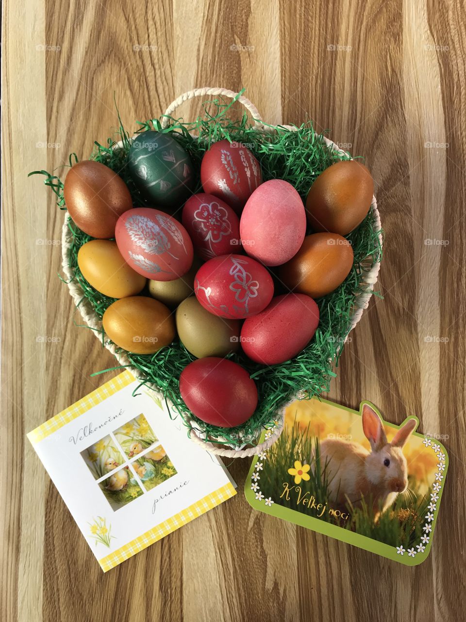 Easter eggs in a basket on a wooden table with easter cards in the Slovak language that are beside basket.