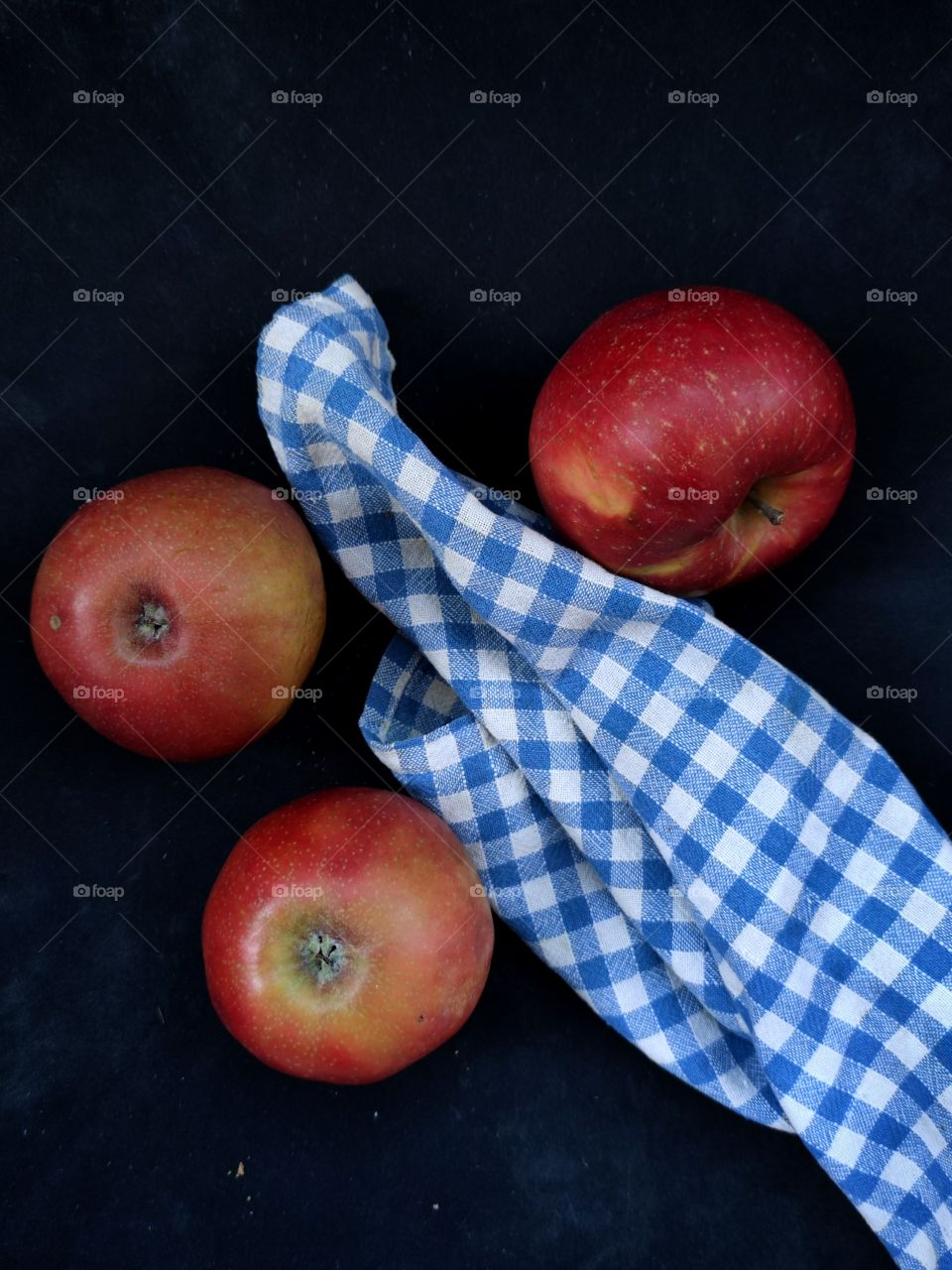 three red apples and a towel in a blue cage on a black background