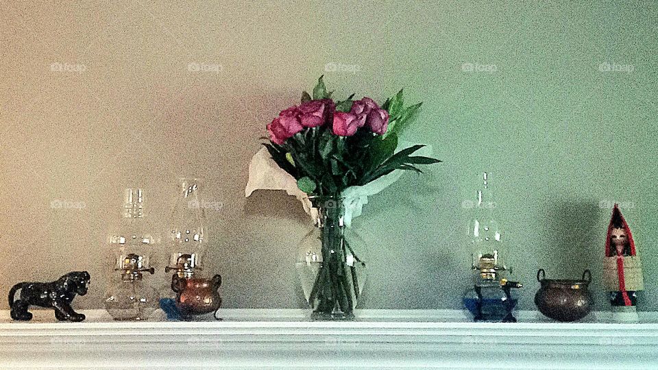 An elegant display with 
roses in a vase, hurricane lamps, and vintage copper urns.