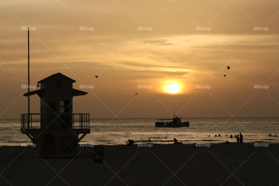 On the beach at sunset, silhouettes of people, boat, birds and lifeguard house 
