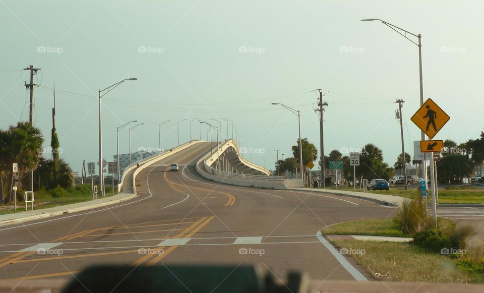 Road trip going towards the beach in central eastern Florida by the Atlantic Ocean meeting some cars on the opposite side of the road, by a curved and nice high bridge with street lights.