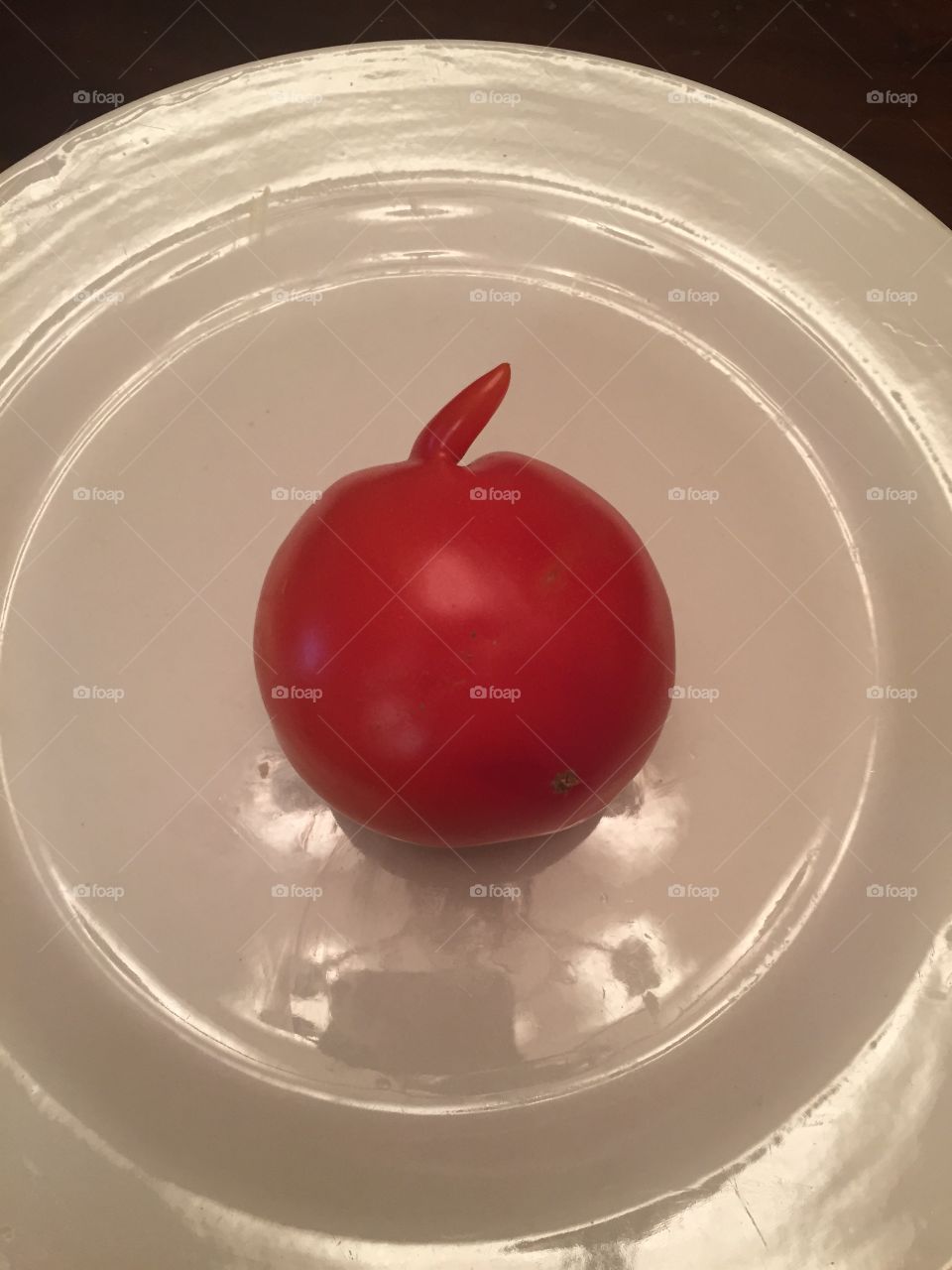 Red tomato with an arm on a white plate.