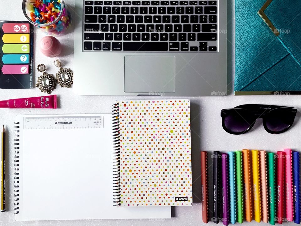 Top view of women's work desk with stationary, laptop, notebook, fashion accessories and empty sketch book.