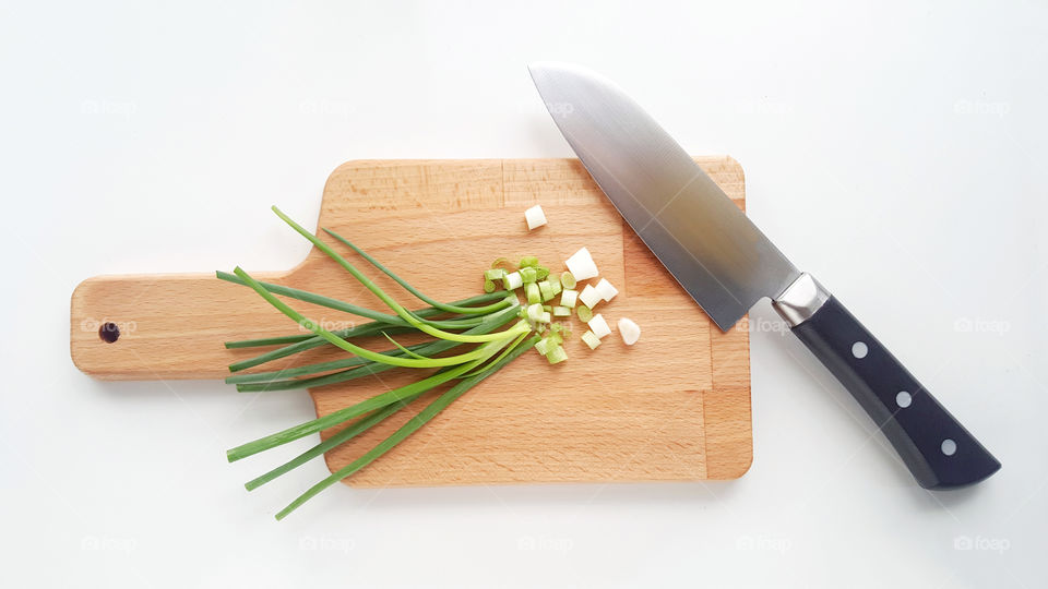 Sliced Scallion (onion leaf) on wooden chopping board with sharp kitchen knife. - Top view, white background