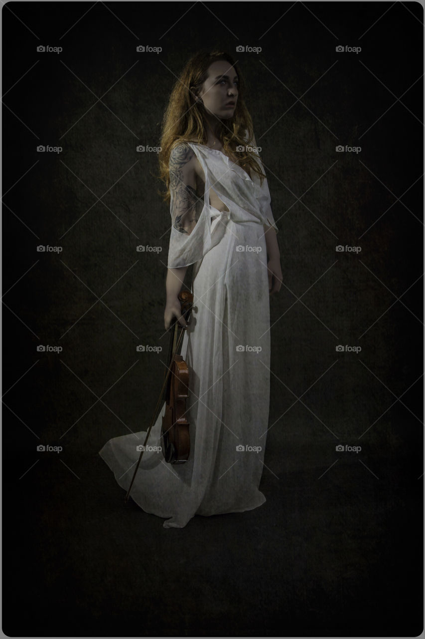 Girl standing in the light. Holding a violin and bow. She is not playing music.