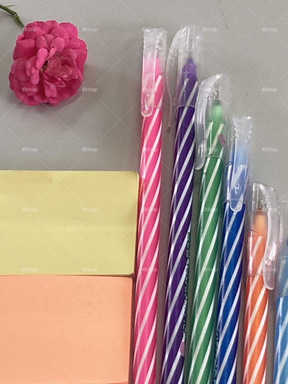Composição com canetas coloridas, blocos de anotações e para alegrar o cenário uma pequena rosa pink.