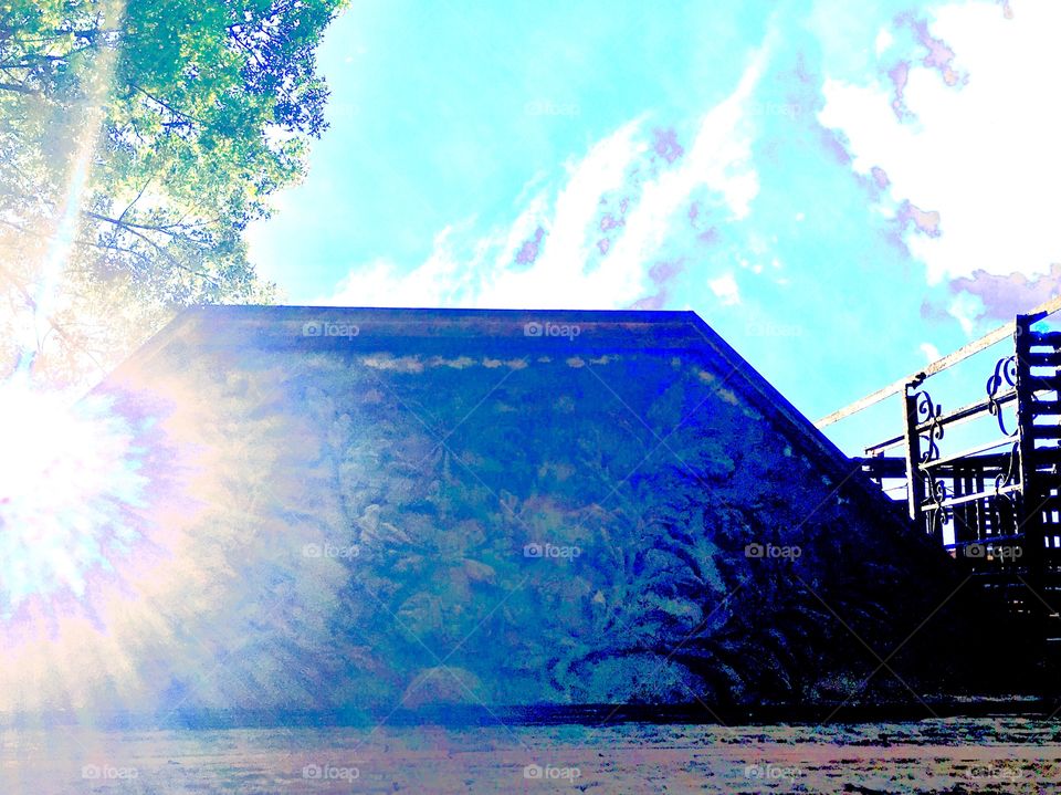 The ornamented wooden awning to a first floor window of  an abandoned building on Waverly Street near Fulton in Forest Green, Brooklyn, New York. Photo was taken in the summer of 2019 looking up into the sky just as the sun cast an interesting flare.