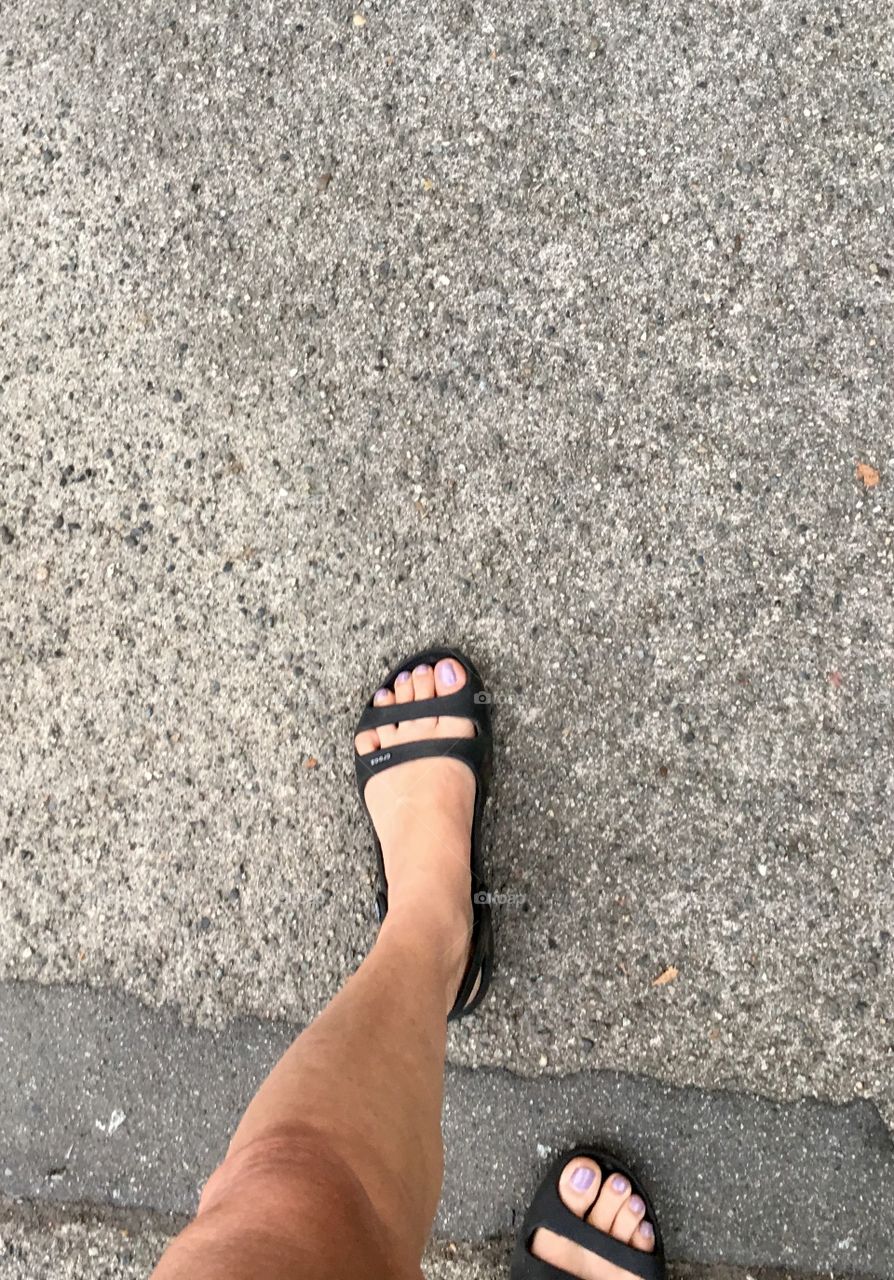 Person's feet in black sandals walking on pavement from above