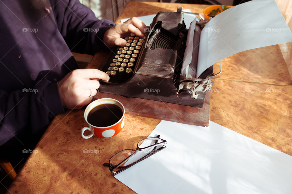A young writer is writing his new book on his old typewriter.