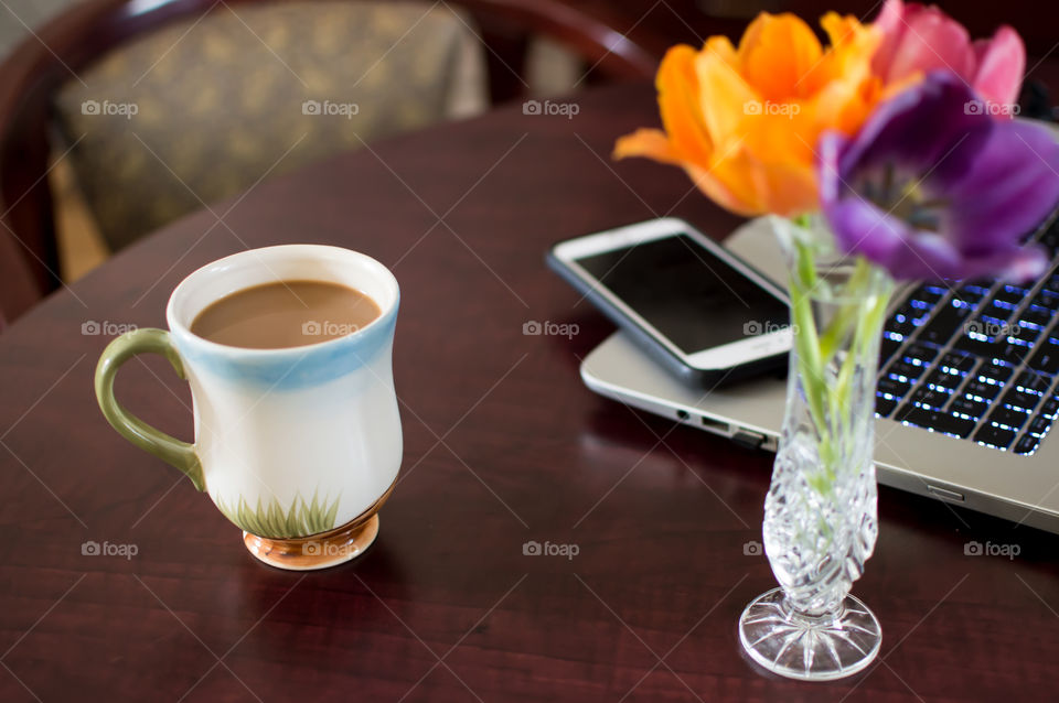 Having a coffee and working conceptual photography, dark wood desktop with laptop computer keyboard and mobile device phone on table near chair 