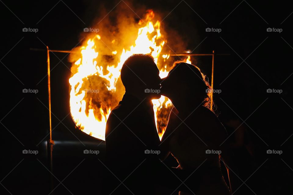 Silhouette of couple kissing near burning heart at night 