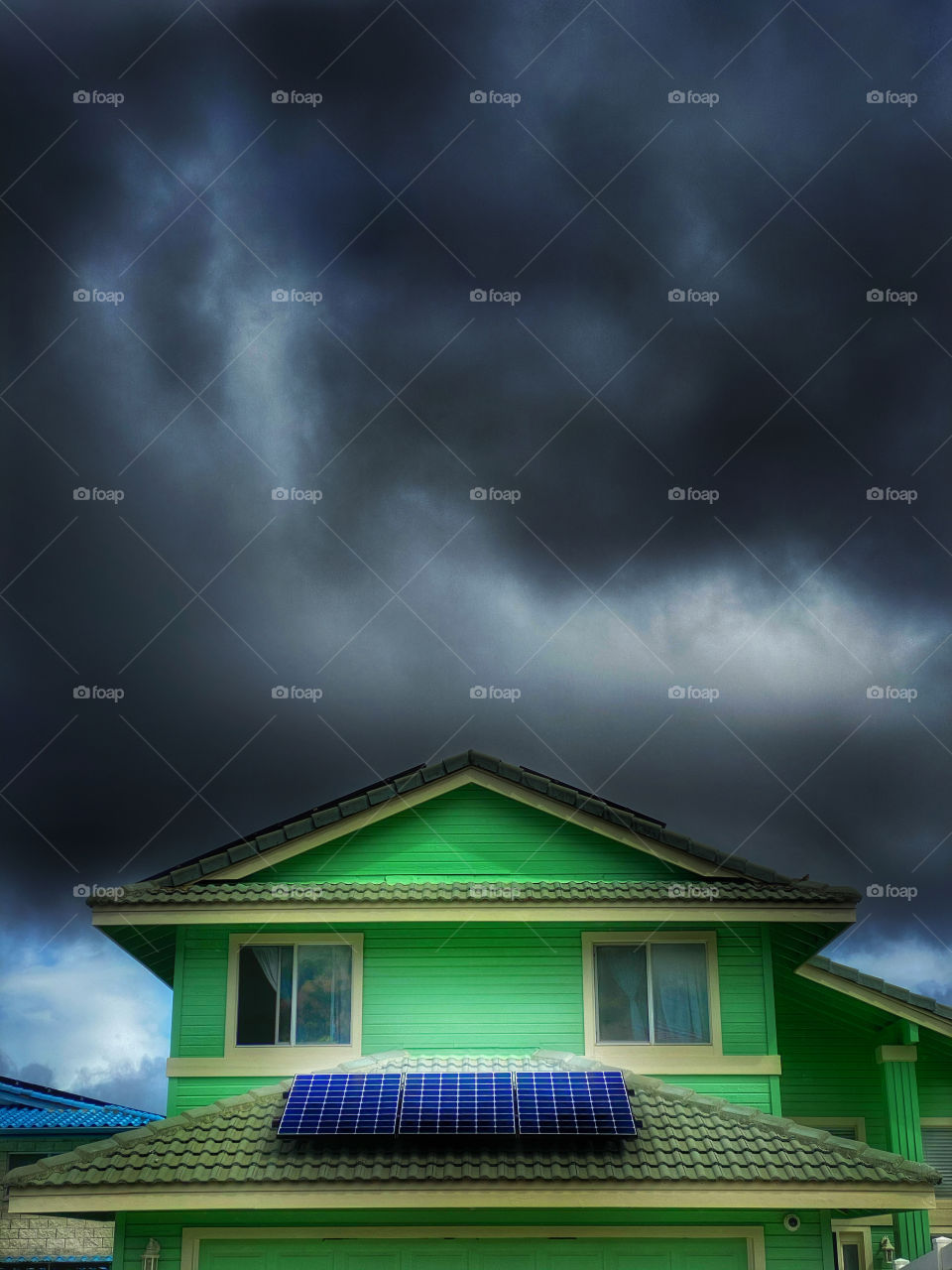 Green house with solar panels on the roof and dark clouds in the sky