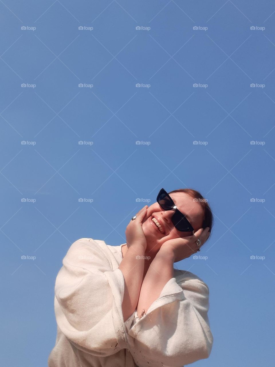 comedy female portrait of a light-skinned girl in sunglasses smiling against a blue sky background