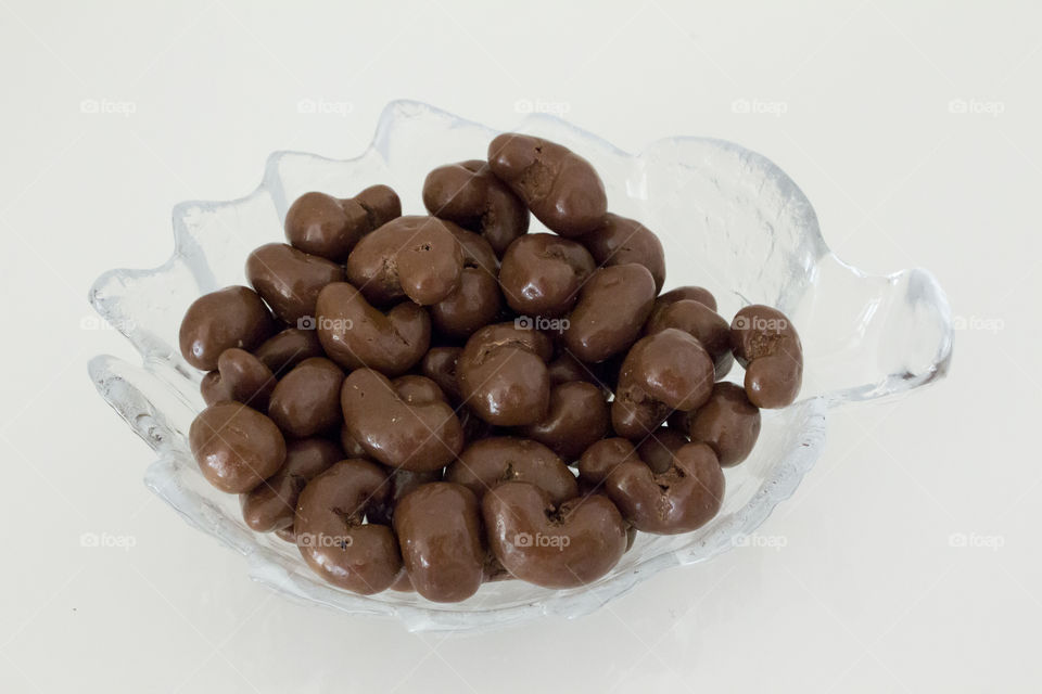 Cashew nuts dipped in chocolate,  lying in a glass bowl shaped like a leaf .