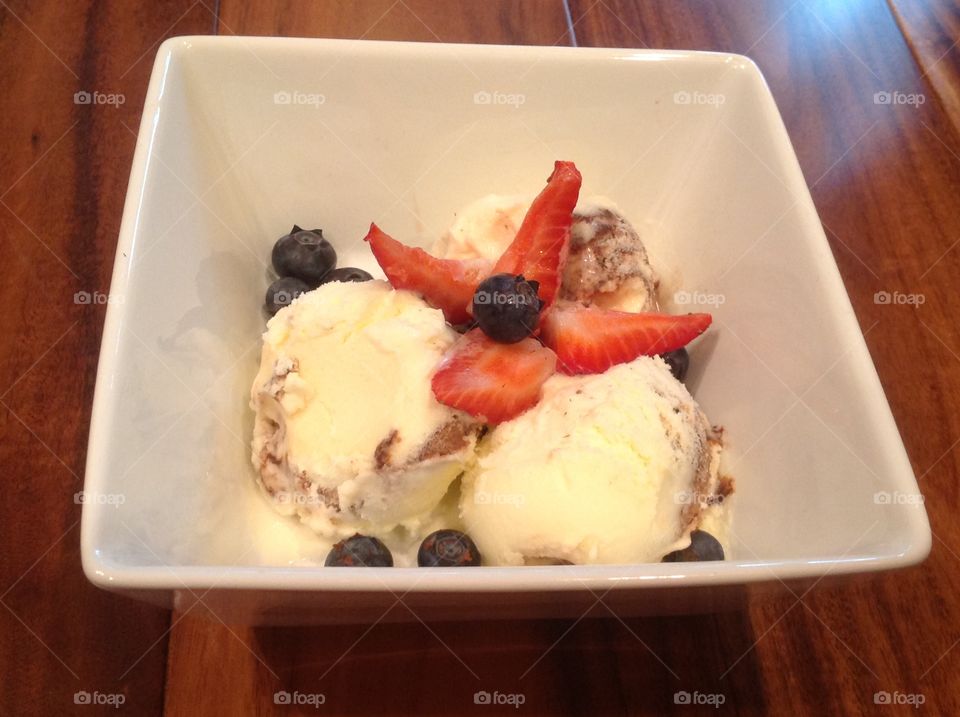 A photo of Vanilla ice cream with strawberries and blueberries. 