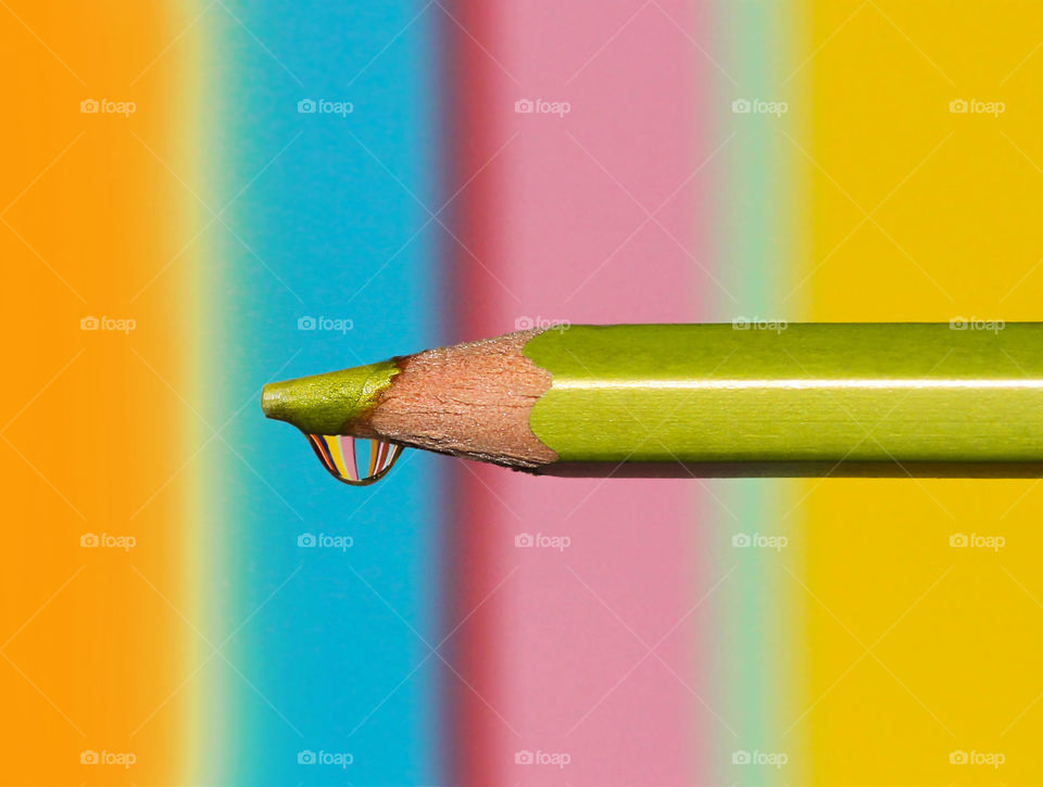 Colorful reflection in a water drop on the top of colored pencil on striped multy colored background