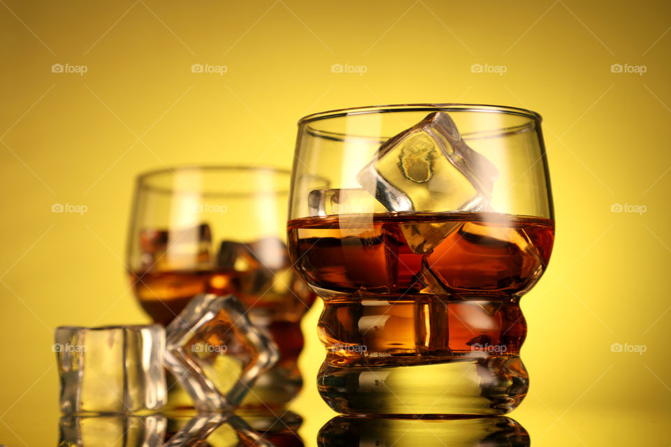 Whiskey glasses with ice cubes on yellow background