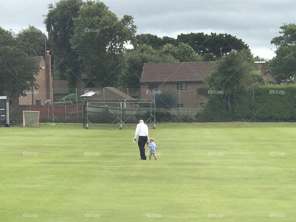 Grandad and grandson walking across cricket ground 2017