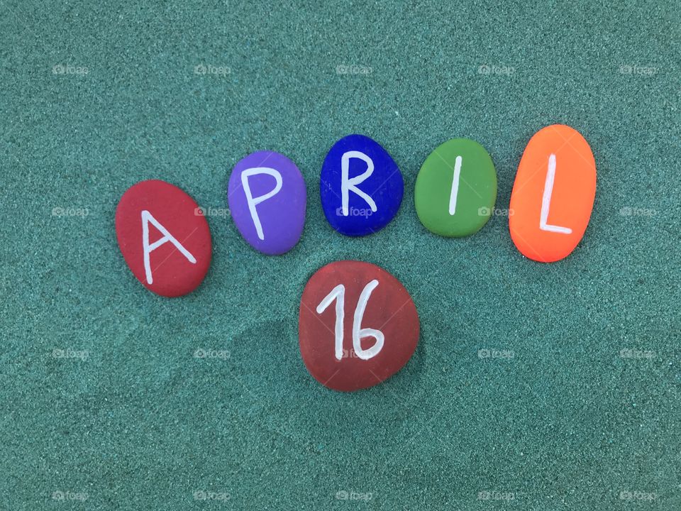 16 April, calendar date with colored stones over green dand 