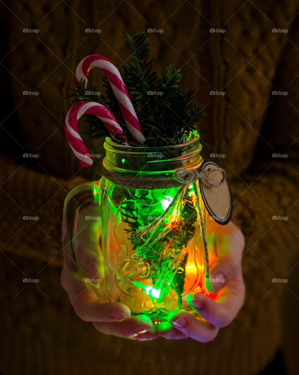 Close up of hands holding a mason jar with Christmas decorations
Close up of hands holding a mason jar with Christmas decorations and light.