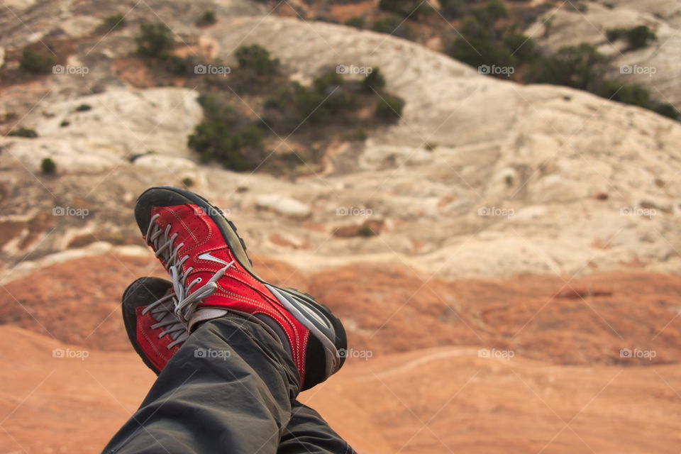 Feet in red shoes hanging over a desert landscape.