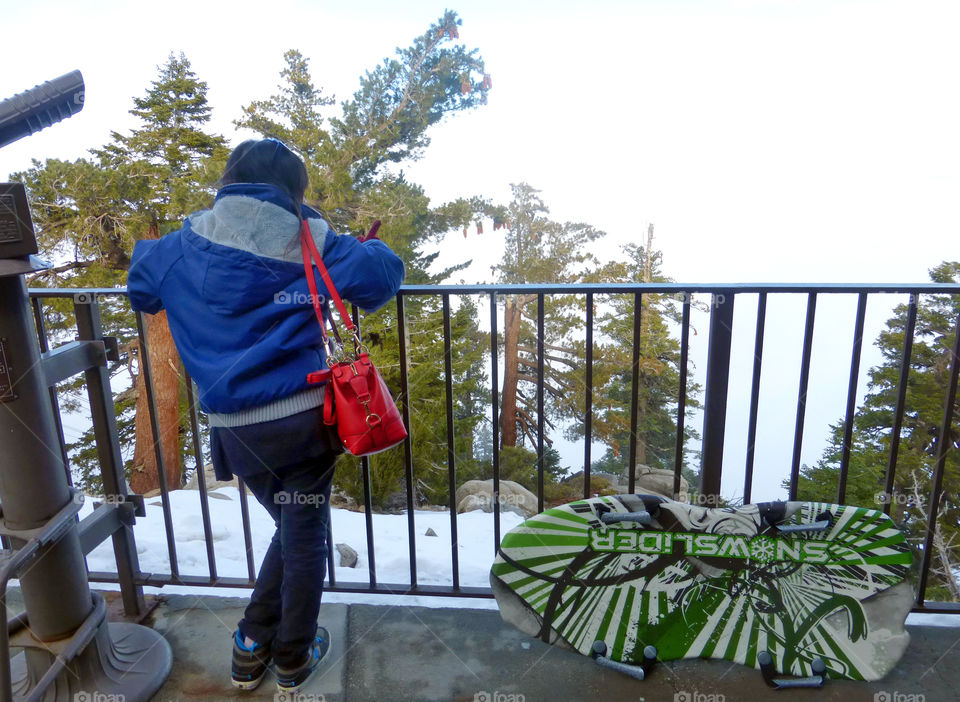 Lady, girl, woman, standing, with a red bag, on viewing deck woth snow sled at the side during winter