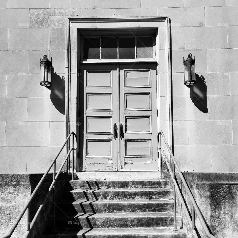 Stairs leading to double doors with rectangles and a transom window in black and white.