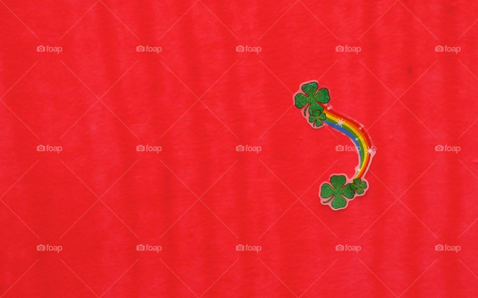 An Irish Rainbow sticker with green shamrocks on a red background.