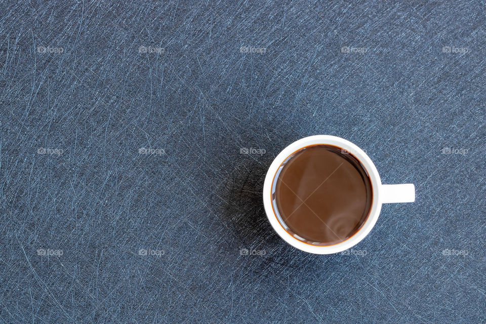 Top view to the white cup with black coffee on the table. Copy space. Minimalistic concept.