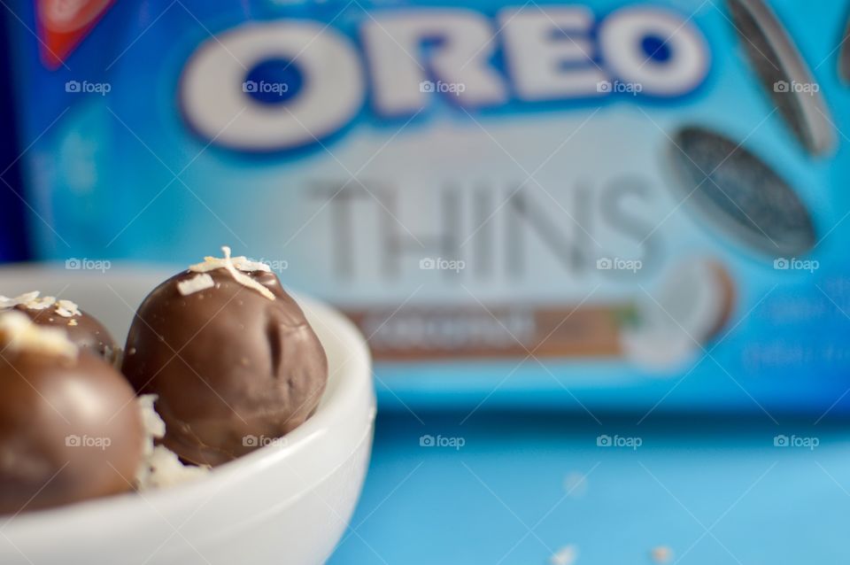 coconut Oreo thin cookies on a blue background with coconut shreds with truffles in a white bowl 