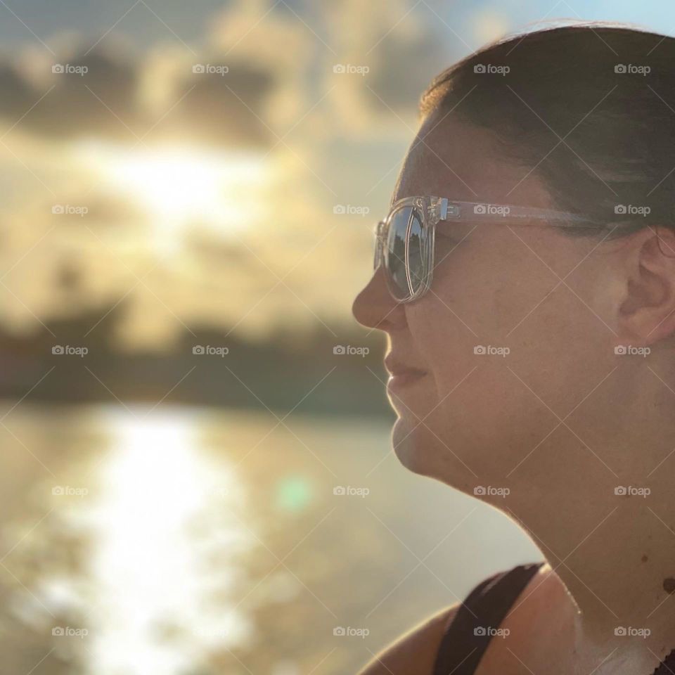 A woman looks off into the sunrise as the sun’s rays reflect off the water. 