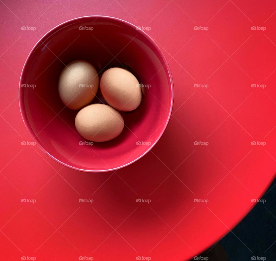 Brown eggs in a red bowl on a red table