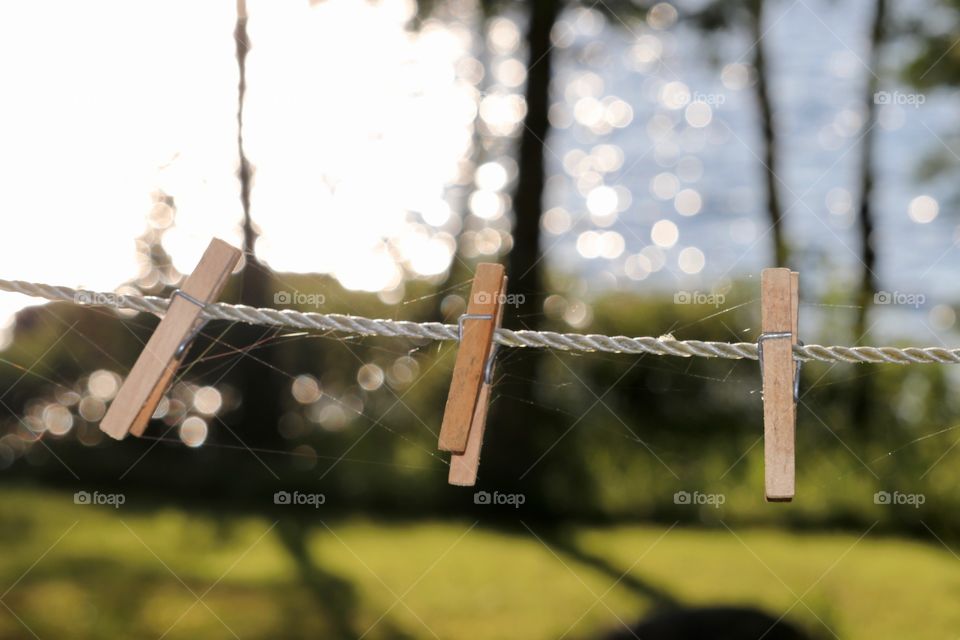 Trio of wood clothesline clothes pegs on outdoor white rope line with lake as backdrop giving off Bokeh effect. Imagery artistic possibility (relationships, love, dating, balance, triple, delicate, fragile, serene,)