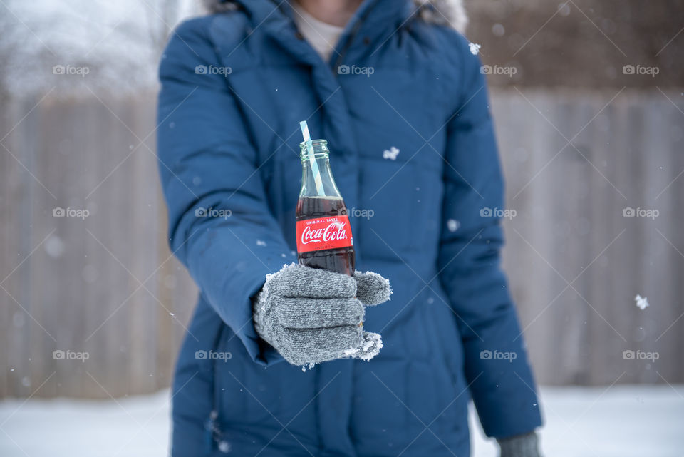 Woman in a winter coat holding out a bottle of Coca-cola outdoors in the snow