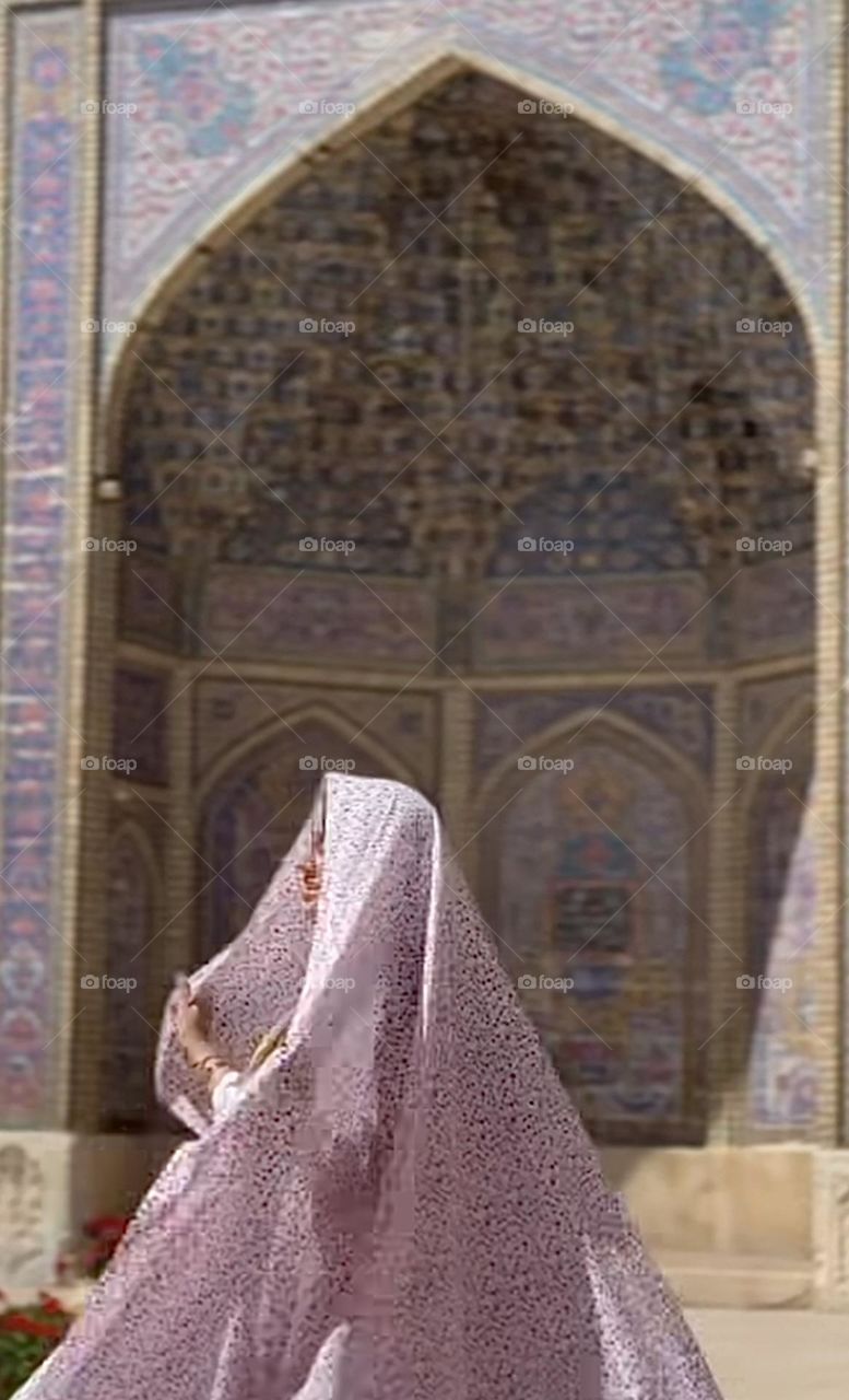 A happy energetic girl with pink bloosoms veil passing through a portico full of patterns of Nasir-al Molk mosque (pink mosque)