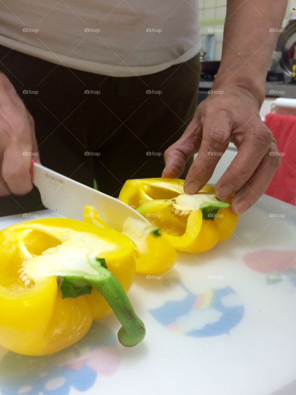 A woman is cutting yellow peppers on the cutting board. 