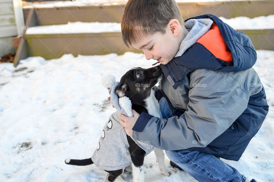 Young boy hugging his new puppy in the snow during winter