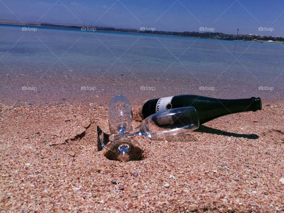 A beautiful beach, sea and seashore in back view with champagne and two champagne glasses on sandy beach in front.