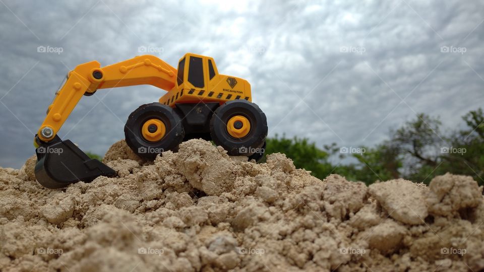 Small but powerful. An orange toy excavator on a pile of stones on a background of dark clouds.