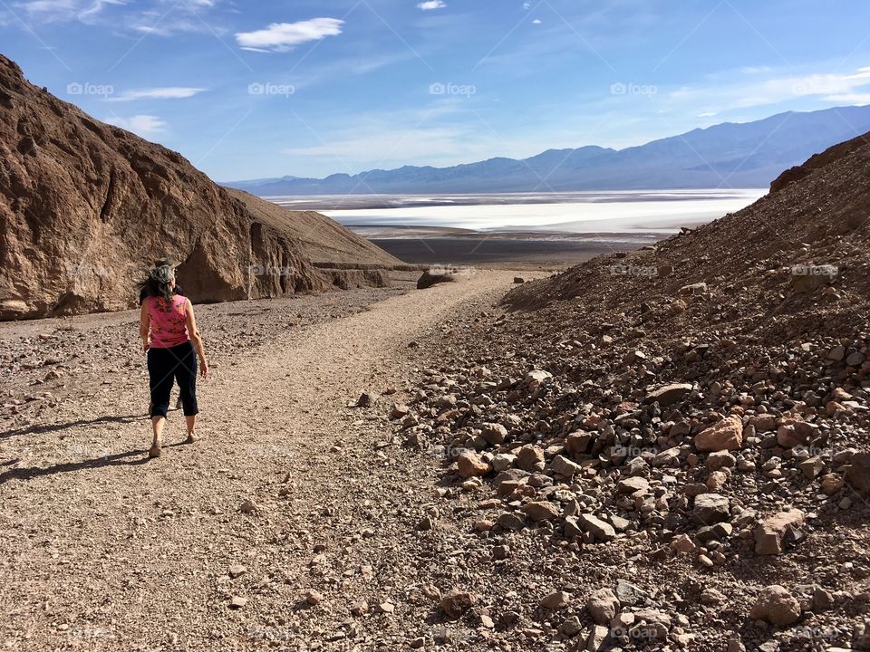 A woman walks along a rocky trail in Nevada, hair blowing in the warm breeze. In the distance, salt flats and mountains appear. 