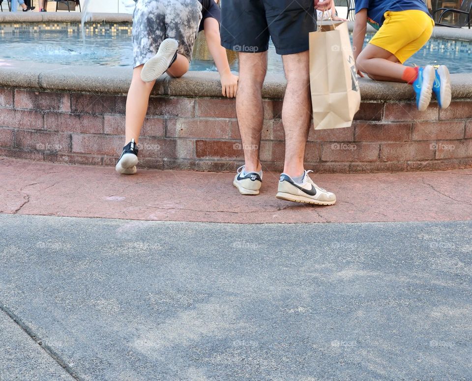 man with shopping bag and two boys wearing shorts dropping coins into a fountain on a Summer evening in Oregon