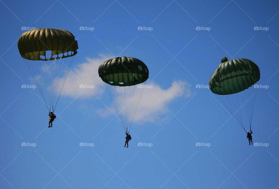WWII battle reenactment of paratroopers parachuting in bright blue sky